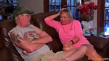 Mature blonde woman is gently sucking her lover's dick while kneeling in front of him